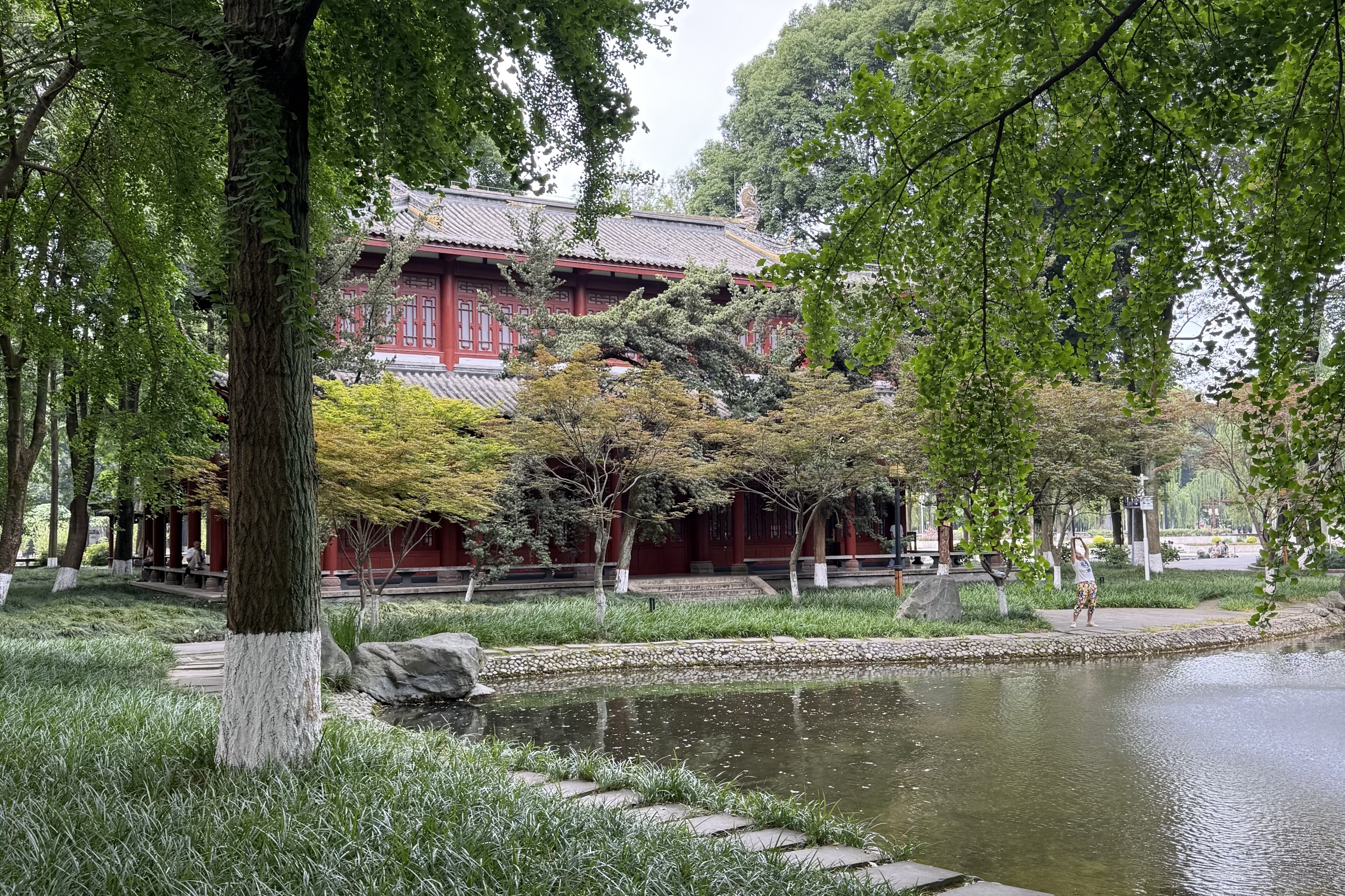 A traditional red building beside a tree-lined pond in Chengdu