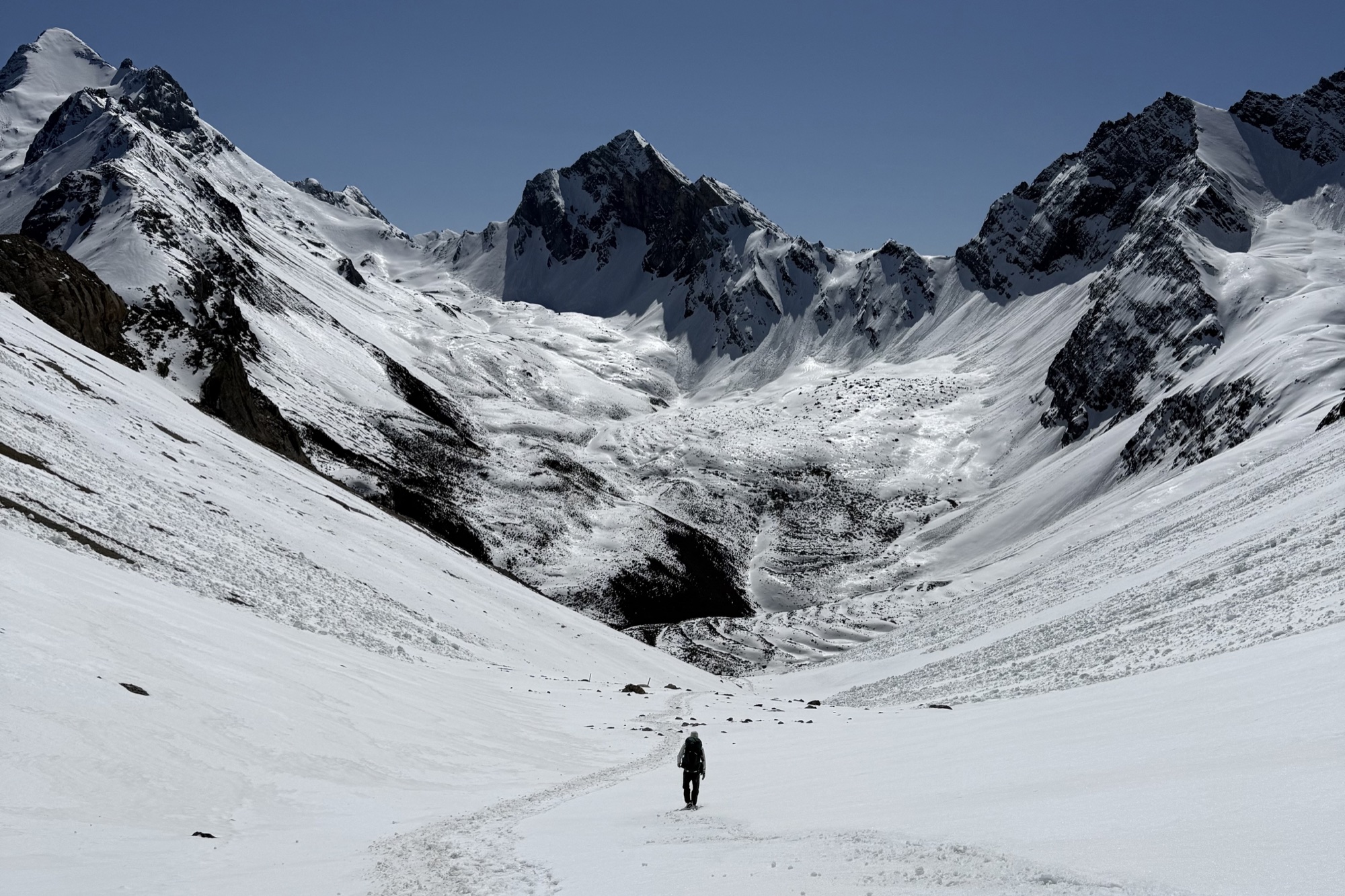 A lone hiker crossing a wide snow-covered mountain valley