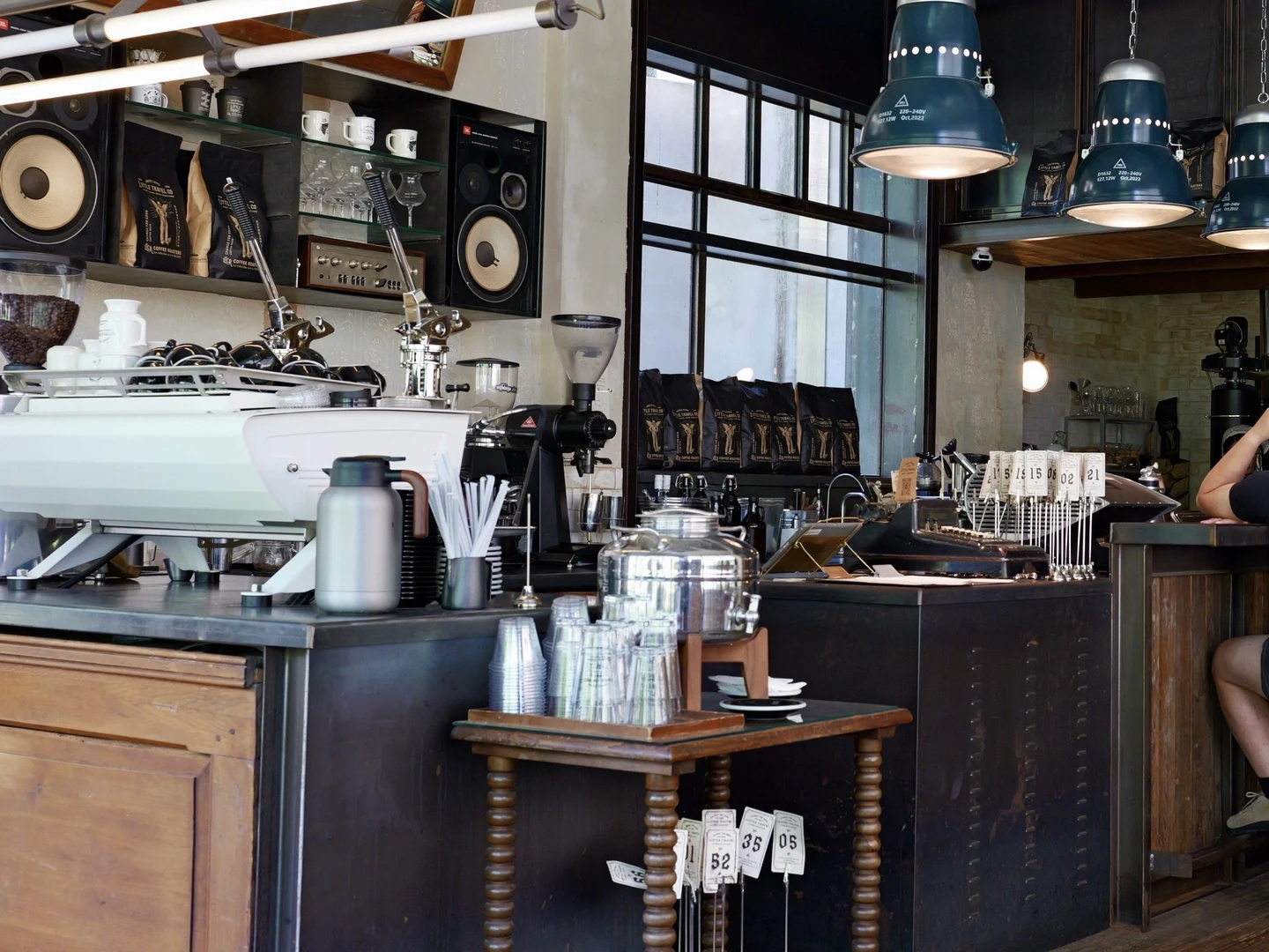 The coffee counter at LittleTravel CPI, with espresso machines, speakers and hanging lamps.