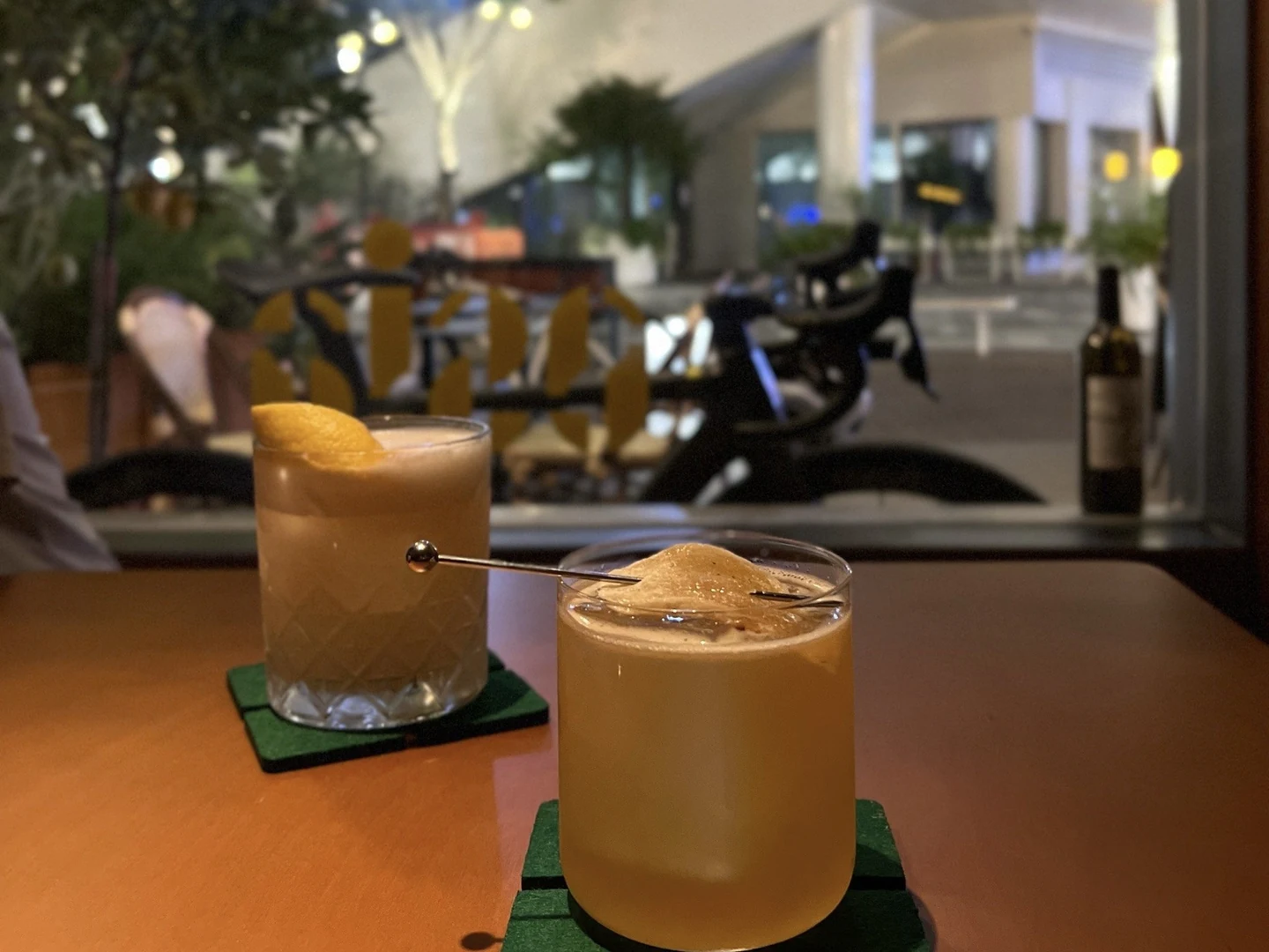 Two cocktails on a wooden table beside the window at O SIA.