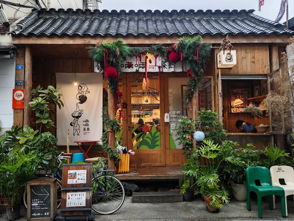 The wooden storefront of 啢啢茶寮, with a tiled roof, plants and outdoor seating