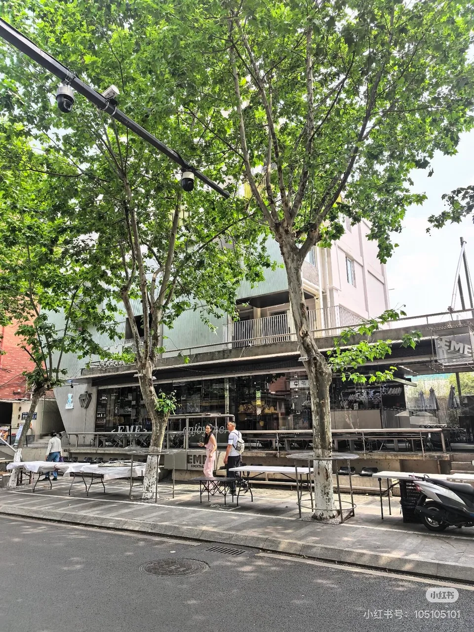 Tree-shaded storefronts and pavement seating along a neighborhood street; original RedNote creator watermark at the lower right