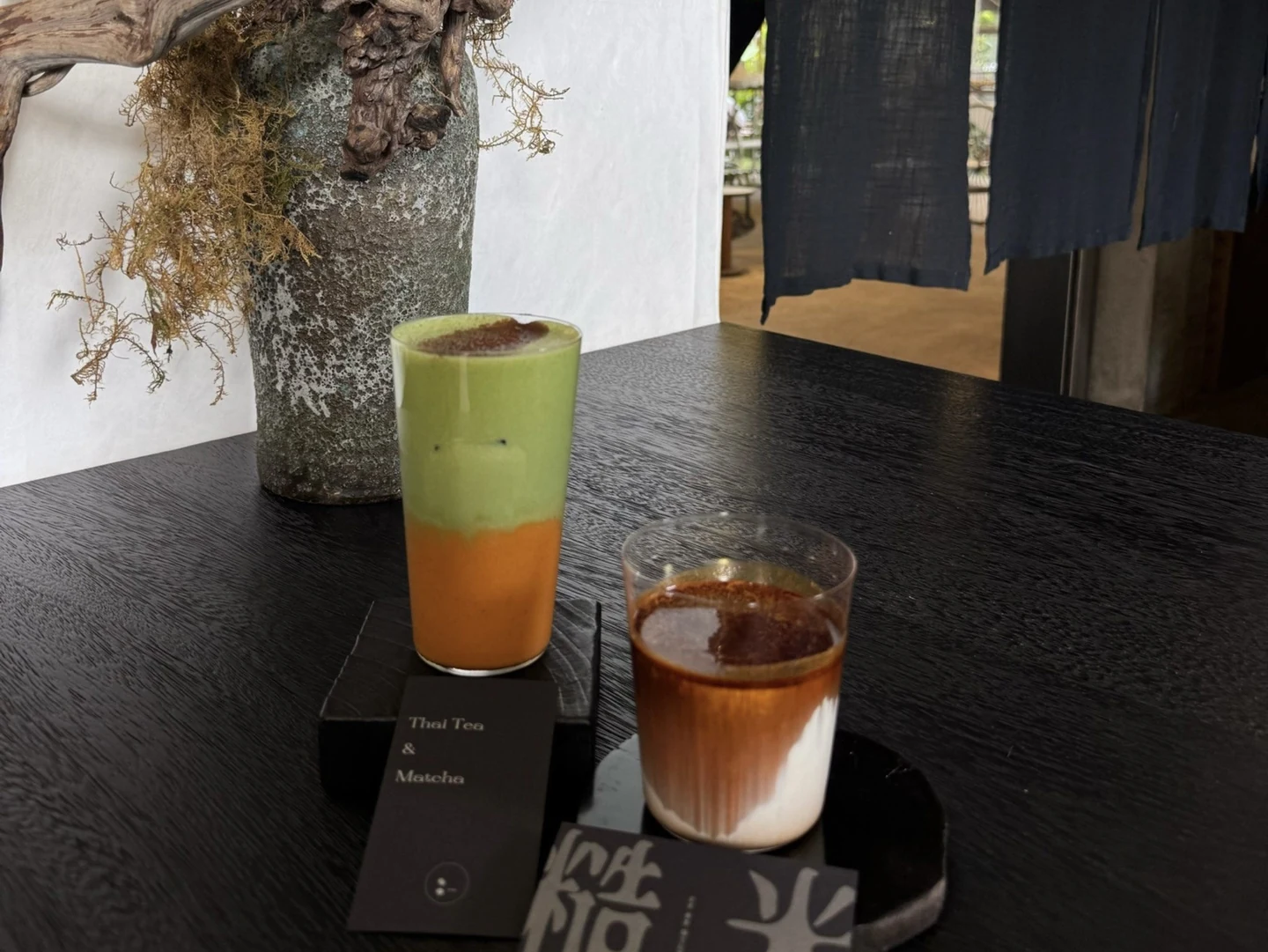 A layered tea and matcha drink beside a coffee on a dark wooden table at Yusuke.