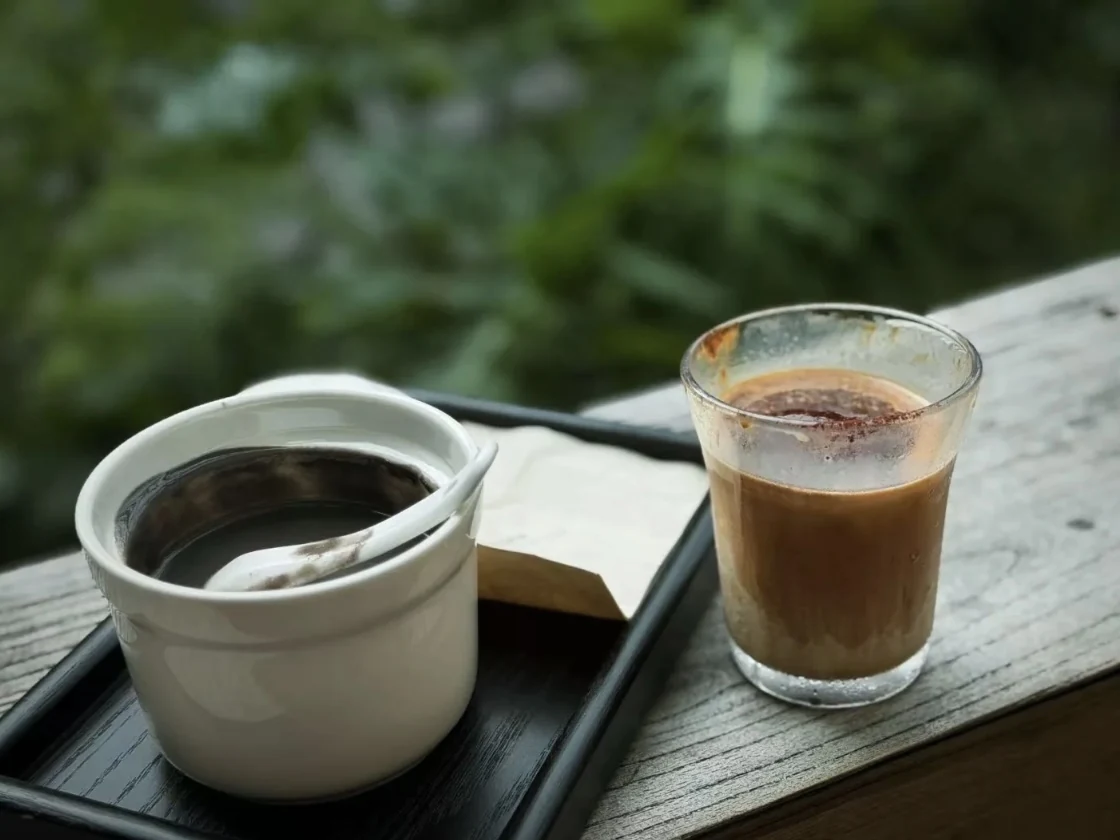 Two coffees by the window at Yusuke, with greenery outside.